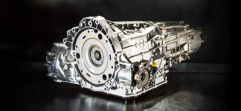 Metallisk motor- och växellådsenhet placerad på mörk yta med svart bakgrund.